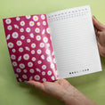 Cargar la imagen en la vista de la galería, Notebook with floral cover and calendar page held by a hand on a green background
