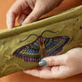 Cargar la imagen en la vista de la galería, Embroidered clutch with a moth design held by hands against an orange background
